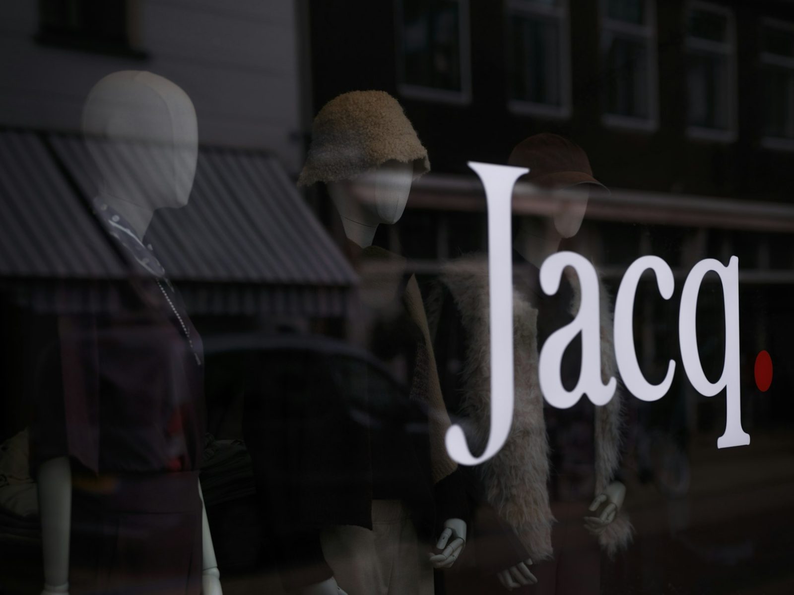 Schaufenster mit großem weißem Schriftzug, dahinter Schaufensterpuppen