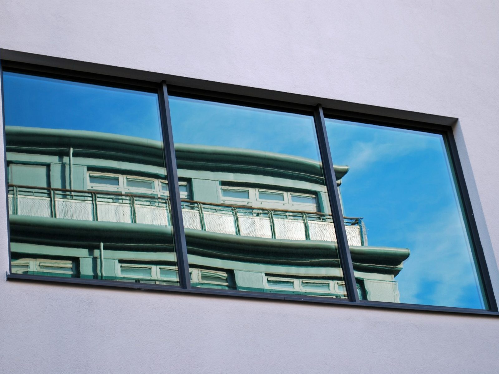 Fenster mit verspiegelter Sonnenschutzfolie, in der sich das Nachbarhaus spiegelt