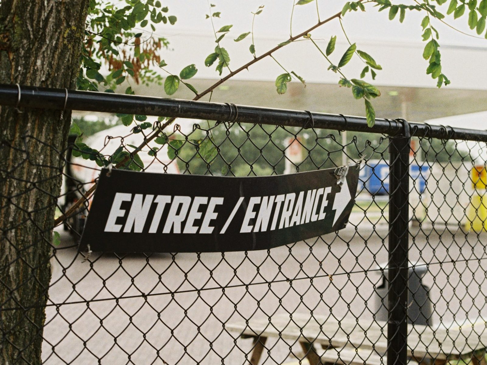 Schwarzes Banner mit Pfeil als Eingangsschild an einem Maschendrahtzaun