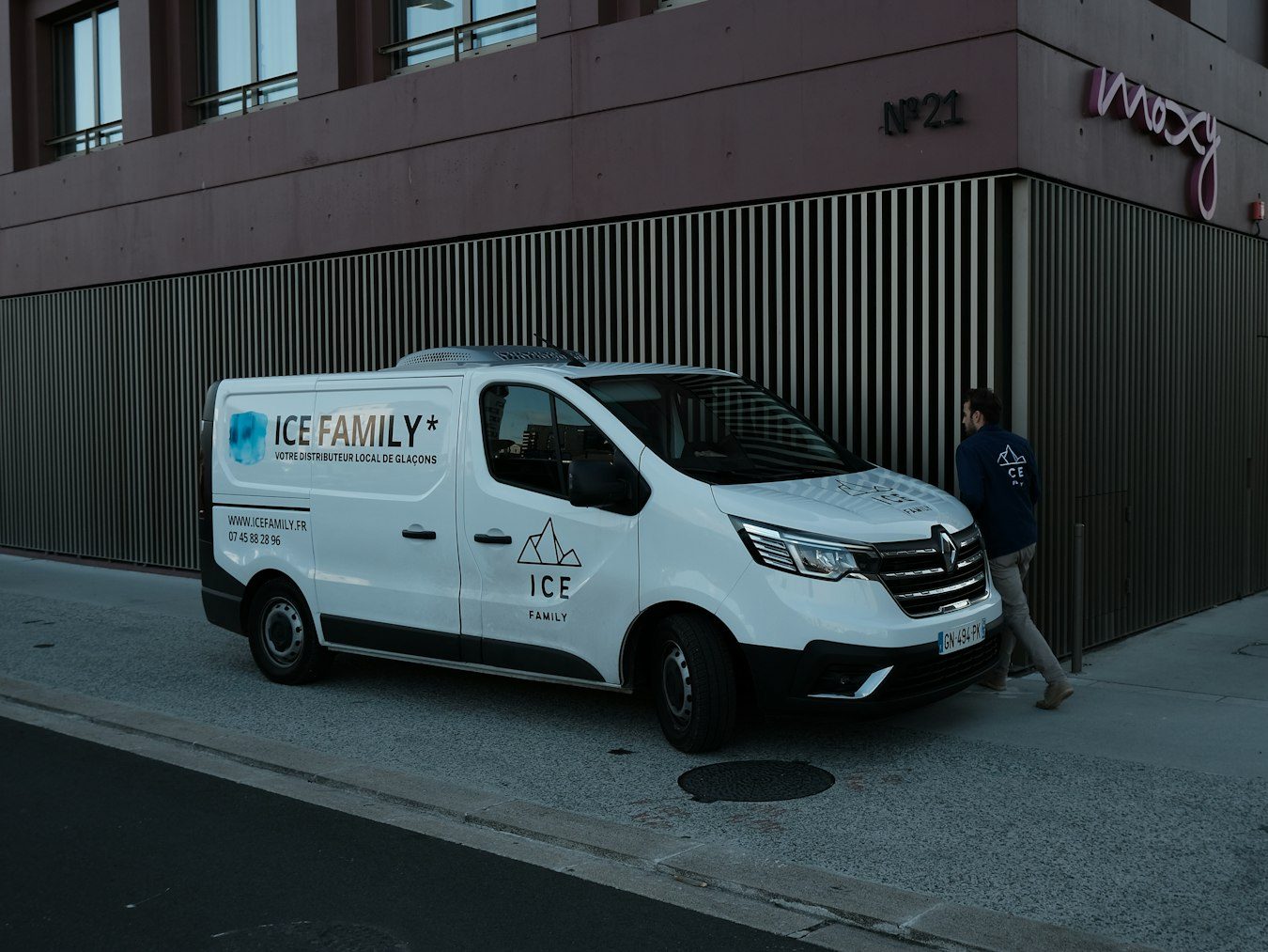 Lieferwagen mit Logo und Kontaktdaten auf Seite und Front vor einem Gebäude