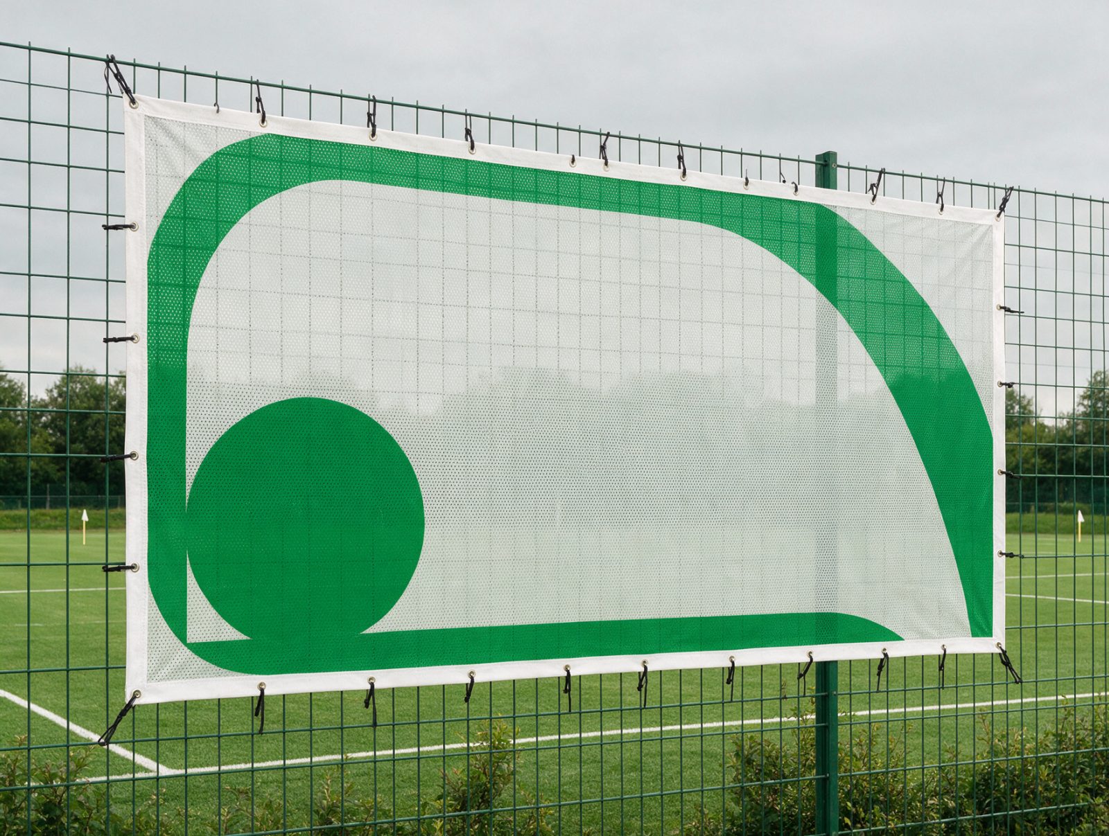 Werbebande mit grünem Beispielmotiv am Zaun eines Sportplatzes, mit Kabelbindern an den Ösen befestigt